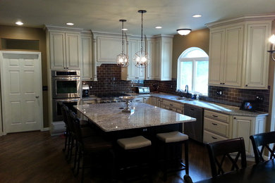 Example of a mid-sized classic l-shaped dark wood floor eat-in kitchen design in St Louis with an undermount sink, raised-panel cabinets, distressed cabinets, granite countertops, brown backsplash, glass tile backsplash and stainless steel appliances