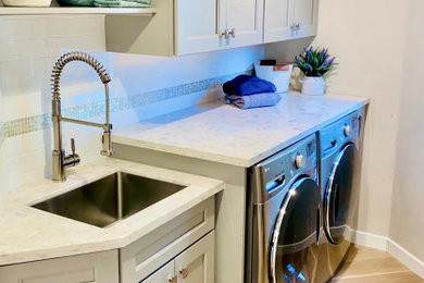 Dedicated laundry room - mid-sized transitional light wood floor dedicated laundry room idea in San Francisco with an undermount sink, shaker cabinets, gray cabinets, quartz countertops, white backsplash, glass tile backsplash, beige walls, a side-by-side washer/dryer and white countertops
