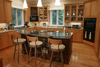 Eat-in kitchen - mid-sized transitional u-shaped medium tone wood floor eat-in kitchen idea in Charlotte with recessed-panel cabinets, an island, an undermount sink, medium tone wood cabinets, granite countertops, beige backsplash, stone tile backsplash and stainless steel appliances