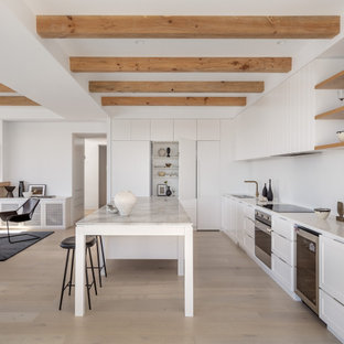 Contemporary open plan kitchen in Sydney with white cabinets, marble benchtops, white splashback, engineered quartz splashback, light hardwood floors, with island, white benchtop and exposed beam.