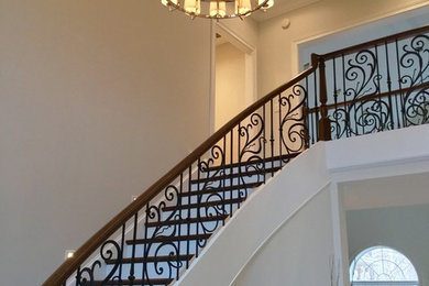 This is an example of an expansive traditional wood curved staircase in Indianapolis with painted wood risers and metal railing.