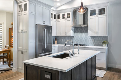 Example of a mid-sized trendy l-shaped medium tone wood floor, brown floor and vaulted ceiling open concept kitchen design in Boise with an undermount sink, shaker cabinets, gray cabinets, quartz countertops, porcelain backsplash, stainless steel appliances, an island, white countertops and blue backsplash