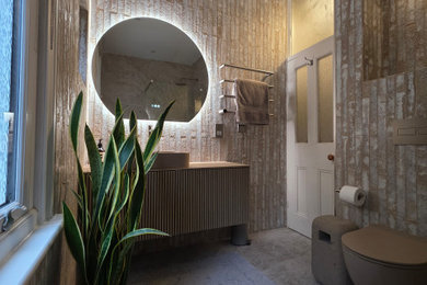 Photo of a medium sized mediterranean family bathroom in London with beaded cabinets, light wood cabinets, a walk-in shower, a wall mounted toilet, beige tiles, ceramic tiles, beige walls, porcelain flooring, a console sink, wooden worktops, beige floors, an open shower, beige worktops, feature lighting, a single sink and a floating vanity unit.