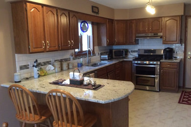 Inspiration for a mid-sized timeless u-shaped beige floor kitchen remodel in Other with an undermount sink, raised-panel cabinets, medium tone wood cabinets, granite countertops, white backsplash, subway tile backsplash, stainless steel appliances and a peninsula