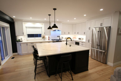 Mid-sized trendy l-shaped light wood floor and beige floor eat-in kitchen photo in Toronto with a farmhouse sink, recessed-panel cabinets, white cabinets, quartz countertops, white backsplash, subway tile backsplash, stainless steel appliances, an island and white countertops