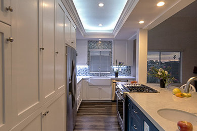 Design ideas for a mid-sized transitional galley open plan kitchen in Los Angeles with a farmhouse sink, shaker cabinets, white cabinets, quartzite benchtops, multi-coloured splashback, glass tile splashback, stainless steel appliances, vinyl floors, with island and multi-coloured floor.