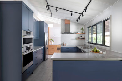Example of a mid-sized transitional u-shaped porcelain tile, gray floor and vaulted ceiling kitchen pantry design in Hawaii with an undermount sink, flat-panel cabinets, blue cabinets, quartz countertops, white backsplash, ceramic backsplash, stainless steel appliances, a peninsula and gray countertops