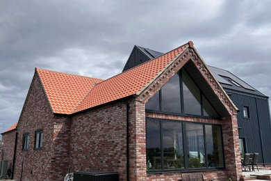 This is an example of a medium sized and multi-coloured modern brick detached house in Other with three floors, a pitched roof, a tiled roof and a red roof.