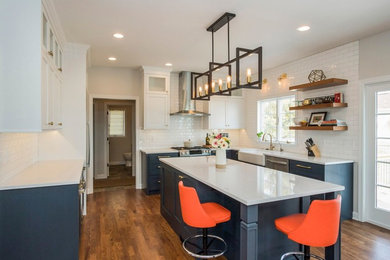 Mid-sized transitional u-shaped kitchen in Chicago with a farmhouse sink, white cabinets, quartz benchtops, white splashback, subway tile splashback, stainless steel appliances, with island, brown floor, shaker cabinets, medium hardwood floors and white benchtop.
