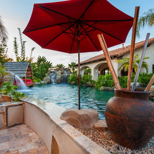 Geräumiger Tropenstil Schwimmteich hinter dem Haus in individueller Form mit Natursteinplatten und Wasserrutsche in San Diego