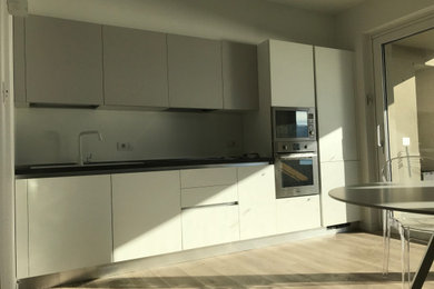 Immagine di una cucina minimalista di medie dimensioni con lavello da incasso, ante lisce, ante bianche, top in laminato, elettrodomestici in acciaio inossidabile, pavimento in gres porcellanato, pavimento beige e top nero