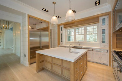 Example of a classic u-shaped medium tone wood floor kitchen design in New York with a farmhouse sink, glass-front cabinets, white cabinets, marble countertops and stainless steel appliances