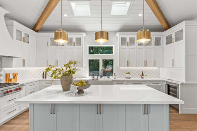 Photo of an expansive modern u-shaped eat-in kitchen in San Francisco with recessed-panel cabinets, white cabinets, quartzite benchtops, white splashback, porcelain splashback, light hardwood floors, brown floor, white benchtop, a farmhouse sink, stainless steel appliances, with island and exposed beam.