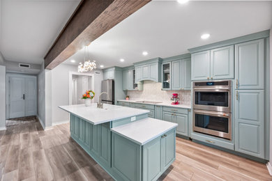 Example of a vinyl floor and brown floor kitchen design in Dallas with an undermount sink, raised-panel cabinets, blue cabinets, quartz countertops, white backsplash, mosaic tile backsplash, stainless steel appliances, an island and white countertops