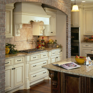 Idées déco pour une grande arrière-cuisine classique en U avec un évier encastré, un placard avec porte à panneau surélevé, des portes de placard blanches, un plan de travail en granite, une crédence en travertin, un électroménager en acier inoxydable, un sol en bois brun et 2 îlots.