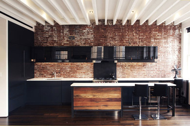Open concept kitchen - small modern single-wall dark wood floor and brown floor open concept kitchen idea in New York with glass-front cabinets, black cabinets, marble countertops, an island, an undermount sink, red backsplash, brick backsplash and black appliances