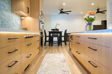 Large world-inspired l-shaped kitchen/diner in San Francisco with a submerged sink, flat-panel cabinets, medium wood cabinets, quartz worktops, metallic splashback, glass tiled splashback, stainless steel appliances, medium hardwood flooring, an island, brown floors and white worktops.