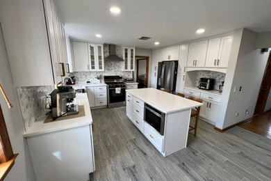 Transitional u-shaped gray floor open concept kitchen photo in New York with shaker cabinets, white cabinets, quartz countertops, white backsplash, marble backsplash, stainless steel appliances, an island and white countertops