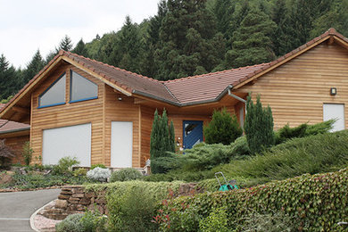 Idée de décoration pour une façade de maison marron en bois de taille moyenne et à un étage avec un toit à deux pans et un toit en tuile.