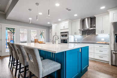 Inspiration for a large transitional l-shaped medium tone wood floor and brown floor open concept kitchen remodel in Dallas with a farmhouse sink, recessed-panel cabinets, blue cabinets, quartzite countertops, black backsplash, marble backsplash, stainless steel appliances, an island and white countertops