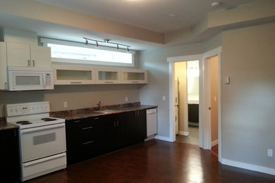 Inspiration for a large contemporary single-wall dark wood floor and brown floor enclosed kitchen remodel in Edmonton with a drop-in sink, shaker cabinets, dark wood cabinets, granite countertops, white appliances and no island