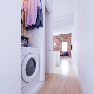 Scandinavian laundry cupboard in DC Metro with white walls, light hardwood flooring and a side by side washer and dryer.