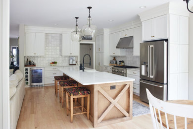 Large transitional l-shaped light wood floor eat-in kitchen photo in Boston with a farmhouse sink, recessed-panel cabinets, white cabinets, quartz countertops, gray backsplash, ceramic backsplash, stainless steel appliances, an island and white countertops