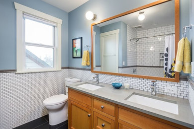 Example of a mid-sized transitional 3/4 white tile and porcelain tile porcelain tile and black floor bathroom design in Portland with shaker cabinets, medium tone wood cabinets, a two-piece toilet, blue walls, an undermount sink and solid surface countertops
