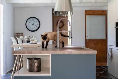 Foto de cocina lineal mediterránea grande cerrada con fregadero encastrado, armarios con paneles lisos, puertas de armario turquesas, encimera de laminado, electrodomésticos de acero inoxidable, suelo de pizarra, una isla, suelo negro y encimeras beige