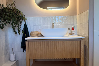 Inspiration for a mid-sized coastal kids' white tile and ceramic tile porcelain tile, multicolored floor and single-sink bathroom remodel in Dorset with furniture-like cabinets, light wood cabinets, a two-piece toilet, pink walls, a vessel sink, solid surface countertops, a hinged shower door, white countertops and a freestanding vanity