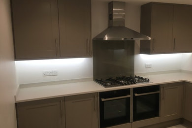 Inspiration for a medium sized modern l-shaped kitchen/diner in Cambridgeshire with a submerged sink, shaker cabinets, grey cabinets, composite countertops, grey splashback, glass sheet splashback, stainless steel appliances, concrete flooring, no island, grey floors and grey worktops.
