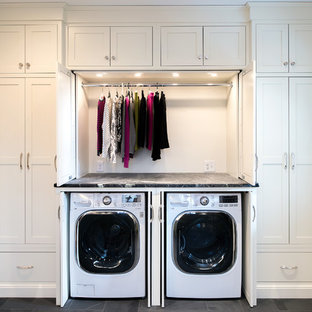 Modelo de lavadero lineal, clásico renovado, grande, con armarios estilo shaker, puertas de armario blancas, encimera de esteatita, suelo de pizarra, lavadora y secadora escondidas, encimeras grises y paredes grises
