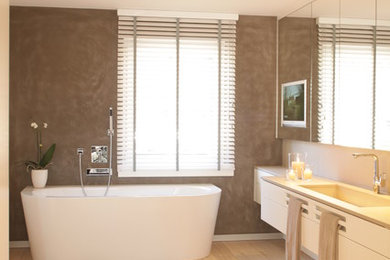 Großes Modernes Badezimmer En Suite mit flächenbündigen Schrankfronten, weißen Schränken, freistehender Badewanne, bodengleicher Dusche, Wandtoilette, beigen Fliesen, Keramikfliesen, beiger Wandfarbe, hellem Holzboden, integriertem Waschbecken, Mineralwerkstoff-Waschtisch, beigem Boden, offener Dusche und beiger Waschtischplatte in Sonstige