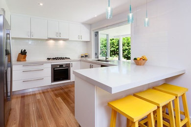 Inspiration for a contemporary kitchen in Sydney with a double-bowl sink, flat-panel cabinets, white cabinets, white splashback, subway tile splashback, stainless steel appliances, medium hardwood floors and a peninsula.