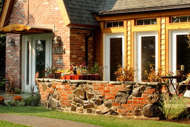 Mid-sized arts and crafts red two-story brick house exterior photo in Seattle with a clipped gable roof and a shingle roof