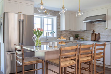 Example of a mid-sized transitional u-shaped vinyl floor and brown floor eat-in kitchen design in Boston with an undermount sink, shaker cabinets, white cabinets, quartz countertops, beige backsplash, ceramic backsplash, stainless steel appliances, an island and beige countertops