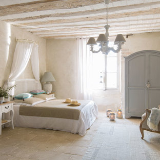 Photo of a mid-sized mediterranean bedroom in London with beige walls, travertine floors, a standard fireplace, a brick fireplace surround and beige floor.