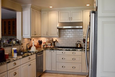 Eat-in kitchen - mid-sized traditional u-shaped porcelain tile and beige floor eat-in kitchen idea in Los Angeles with a drop-in sink, raised-panel cabinets, white cabinets, granite countertops, white backsplash, subway tile backsplash, stainless steel appliances and multicolored countertops
