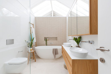 Photo of a large modern master bathroom in Sydney with furniture-like cabinets, brown cabinets, a freestanding tub, a corner shower, a wall-mount toilet, beige tile, subway tile, white walls, travertine floors, a vessel sink, engineered quartz benchtops, beige floor, a hinged shower door, white benchtops, a niche, a double vanity, a floating vanity and vaulted.