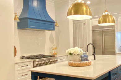 ローリーにあるトランジショナルスタイルのおしゃれなアイランドキッチン (エプロンフロントシンク、シェーカースタイル扉のキャビネット、白いキャビネット、クオーツストーンカウンター、白いキッチンパネル、セラミックタイルのキッチンパネル、シルバーの調理設備、無垢フローリング、茶色い床、白いキッチンカウンター) の写真