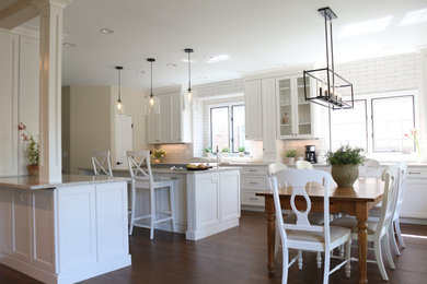 Example of a mid-sized transitional dark wood floor and brown floor eat-in kitchen design in Denver with a farmhouse sink, flat-panel cabinets, white cabinets, quartzite countertops, white backsplash, porcelain backsplash, paneled appliances, an island and beige countertops