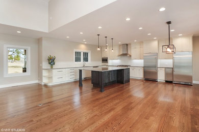 Huge transitional l-shaped medium tone wood floor open concept kitchen photo in Chicago with an undermount sink, raised-panel cabinets, white cabinets, granite countertops, white backsplash, subway tile backsplash, stainless steel appliances and an island