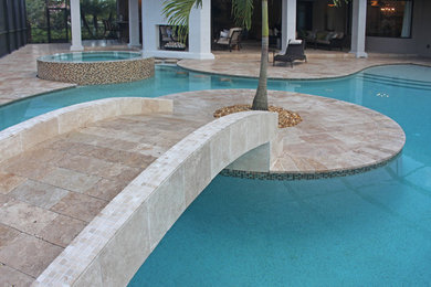 Photo of a tropical backyard custom-shaped natural pool in Tampa with a hot tub and natural stone pavers.