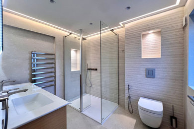 Large contemporary grey and cream family bathroom in London with medium wood cabinets, a walk-in shower, a wall mounted toilet, beige tiles, beige walls, porcelain flooring, beige floors, a feature wall, double sinks, flat-panel cabinets, an alcove bath, ceramic tiles, a built-in sink, an open shower and a floating vanity unit.