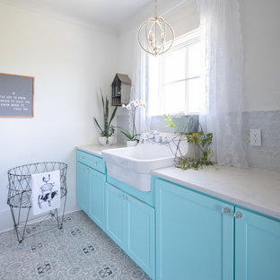 Foto de cuarto de lavado lineal, campestre, de tamaño medio, con fregadero sobremueble, armarios estilo shaker, puertas de armario azules, encimera de cuarzo compacto, paredes blancas, suelo de baldosas de cerámica, lavadora y secadora juntas, suelo gris y encimeras blancas