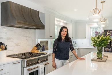 Huge transitional l-shaped medium tone wood floor and gray floor eat-in kitchen photo in New York with a farmhouse sink, shaker cabinets, white cabinets, quartz countertops, white backsplash, marble backsplash, white appliances, an island and white countertops