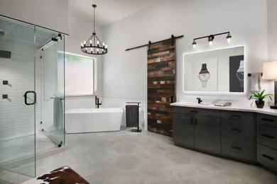 Photo of an industrial master bathroom in Phoenix with flat-panel cabinets, grey cabinets, a freestanding tub, a corner shower, white tile, porcelain tile, grey walls, cement tiles, an undermount sink, engineered quartz benchtops, grey floor, a hinged shower door and white benchtops.