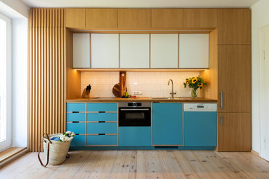 Einzeilige, Mittelgroße Moderne Wohnküche mit Küchenrückwand in Weiß, Rückwand aus Porzellanfliesen, brauner Arbeitsplatte, blauen Schränken und Arbeitsplatte aus Holz in München