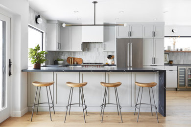 Inspiration for a scandinavian u-shaped kitchen in Los Angeles with shaker cabinets, grey cabinets, grey splashback, stainless steel appliances, light hardwood floors, a peninsula, beige floor and black benchtop.