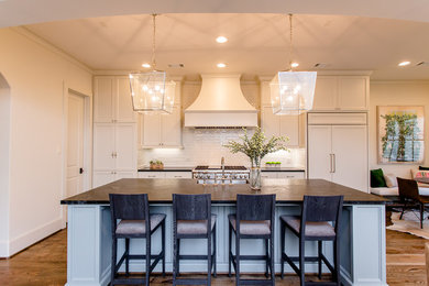 Inspiration for a mid-sized transitional galley open plan kitchen in Houston with a farmhouse sink, recessed-panel cabinets, beige cabinets, soapstone benchtops, beige splashback, subway tile splashback, panelled appliances, dark hardwood floors and with island.